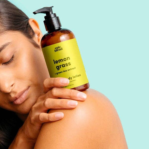 Woman holding a bottle of lemon grass body lotion against a light blue background