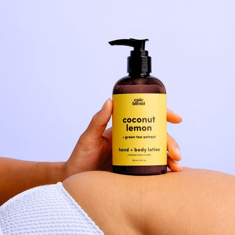 Hand holding a bottle of 'Epic Blend' coconut lemon hand and body lotion against a light purple background